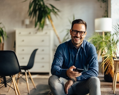 A smiling male entrepreneur sits in a bright workspace holding a phone, representing Veterans Florida's Growth Cohort helping veteran founders scale revenue and grow their teams in Florida.